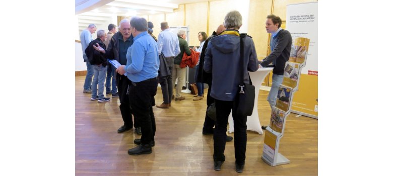 Die Verbraucherzentrale mit einem Informationsstand ist links im Bild zu sehen, im Hintergrund sind Bürgerinnen und Bürger in ein Gespräch verwickelt.